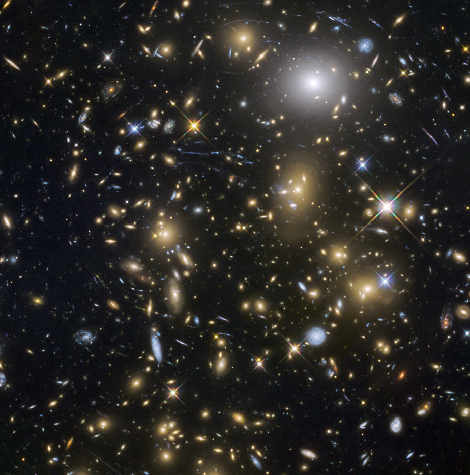 The colored image shows the vastness of our universe. In front of a black background, many luminous spots in yellow, blue and white can be seen, some of which look like stars, others like spiral galaxies.