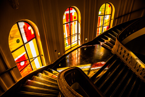The photo shows the colored windows bathing the Main Building’s stairwells in yellow and orange light.